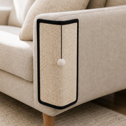 CornerClaw natural sisal scratch pad installed on a cream sofa arm with a pom-pom hanging from the top